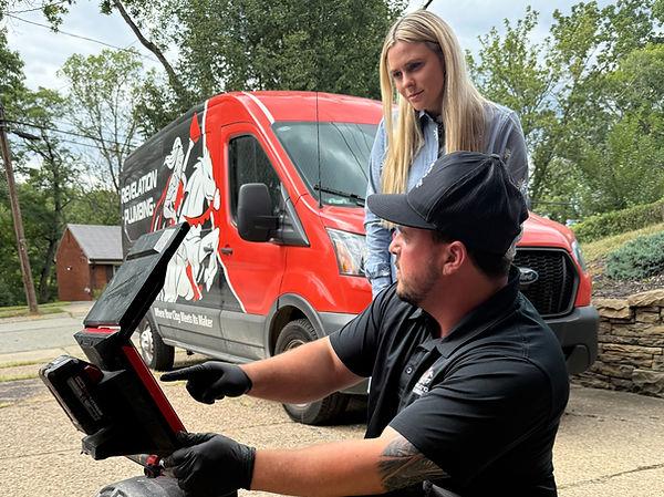 Revelation Plumbing technician showing a Pittsburgh homeowner a sewer camera reading beside the company van